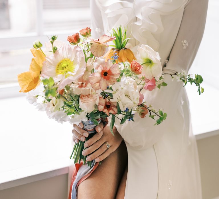 Bride holds bright & bold pastel bouquet tied with ribbon and wears pearl jewellery 