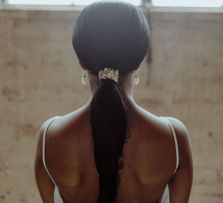 A bride stands with her back to the camera to show her long hair held back in a low ponytail for a simple elegant wedding.