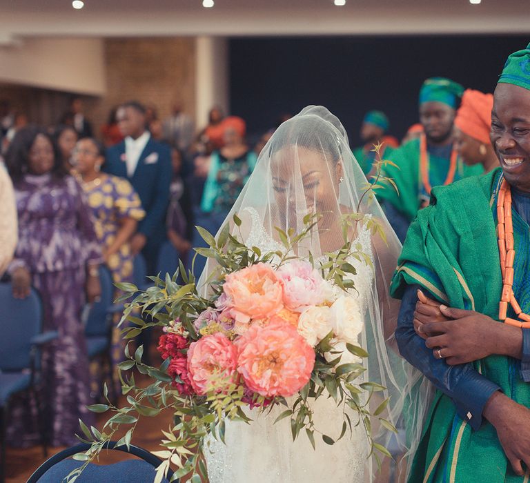 Bride walks down the aisle whilst holding bouquet filled with large peonies