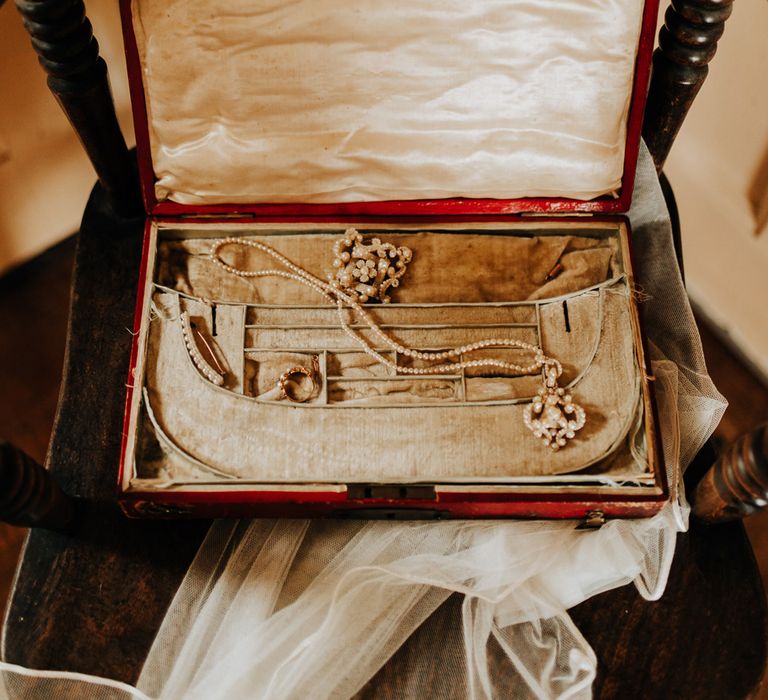 Pearl necklace in red box resting on wooden chair and veil before garden wedding reception