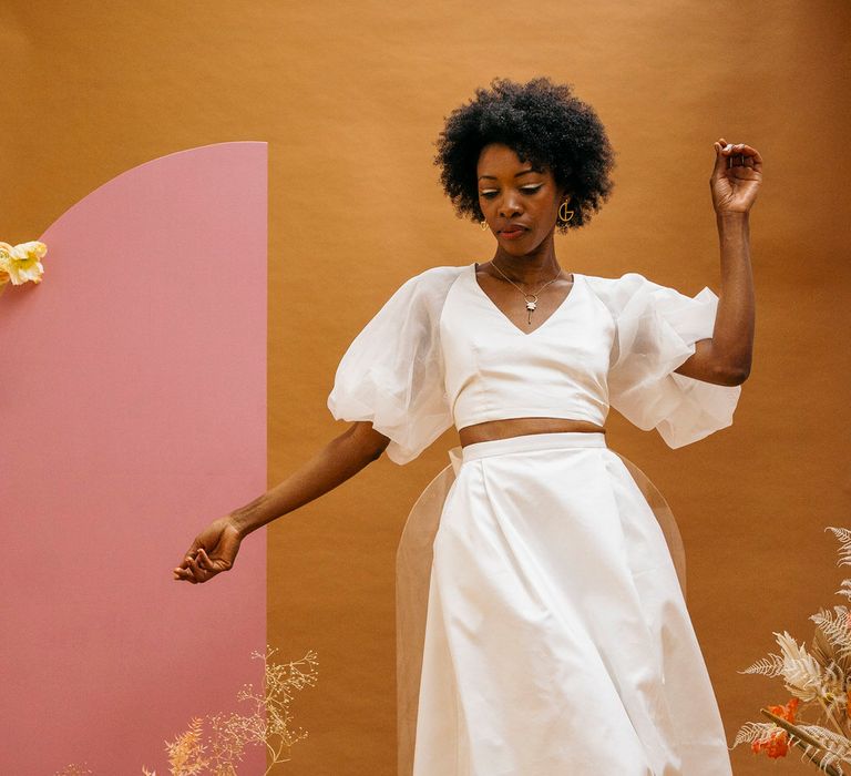 Bride wearing sleek minimal wedding separates; a puff sleeve top and long maxi skirt. Next to neutral colour dried flowers