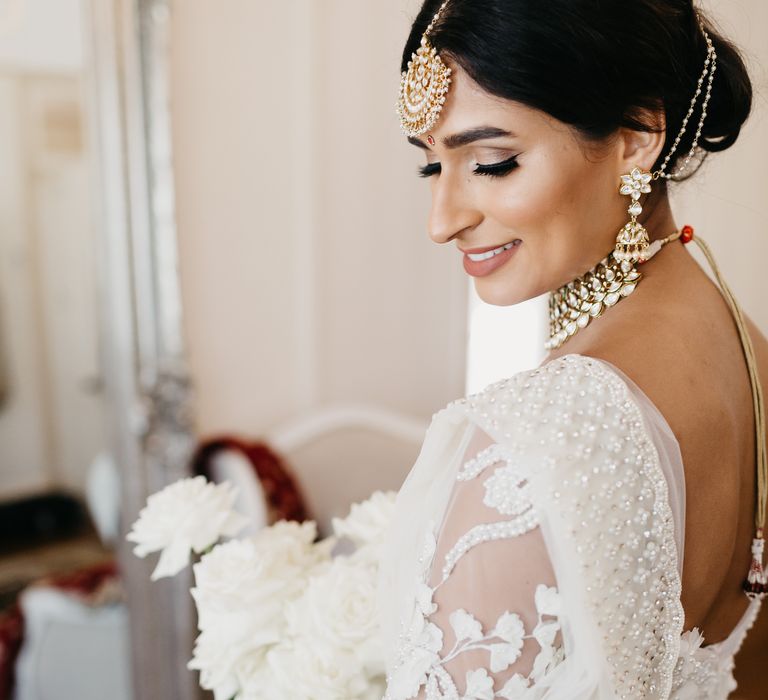 Bride looks down and smiles as she wears white traditional saree for her wedding day