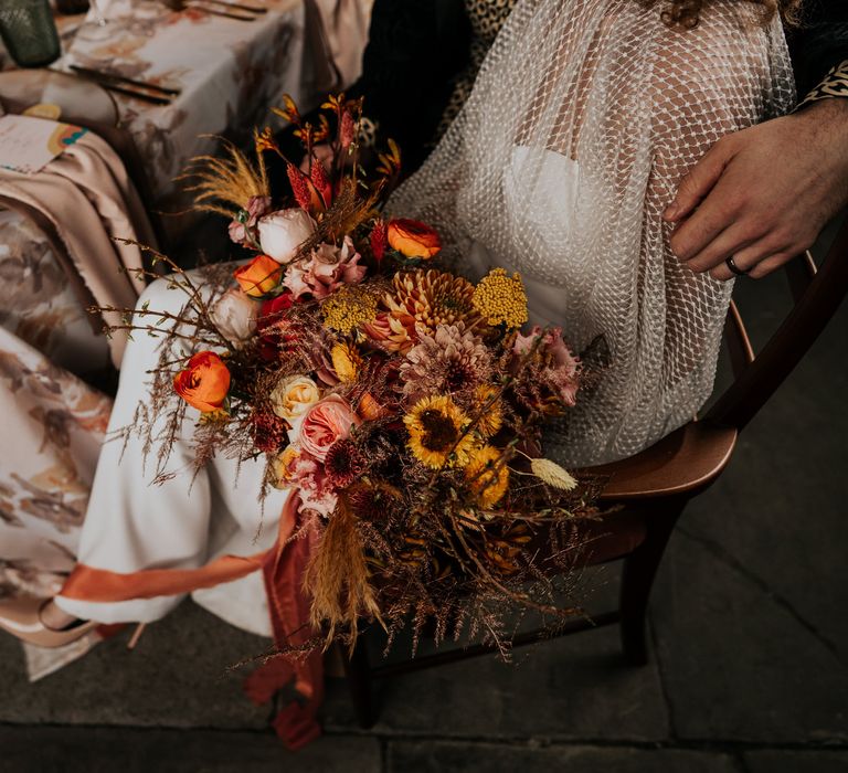 Orange and yellow wedding bouquet with fresh and dried flowers including roses, ranunculus, daisies and dahlias