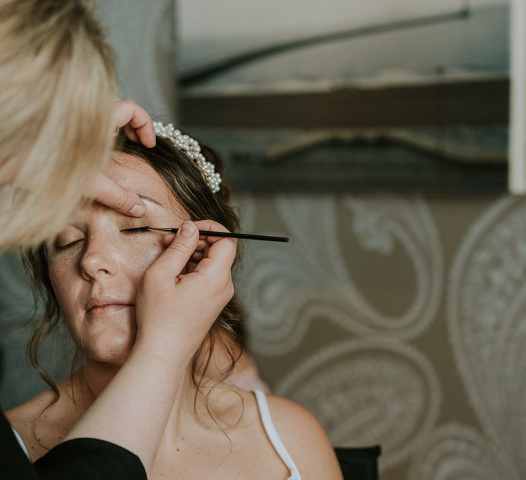 Bride has her eye makeup done on the morning of her wedding as she wears bridal crown