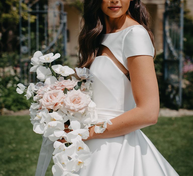 Bride in a strapless princess wedding dress with removable cape holding an white rose and orchid wedding bouquet 