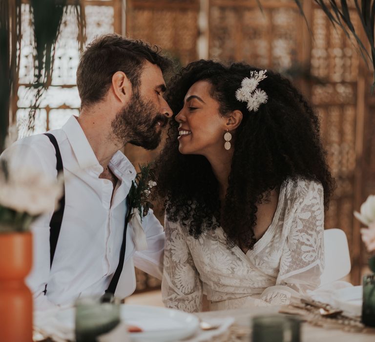 Groom in an open collar shirt and braces kissing his bride with afro hair in a Yolan Cris wedding dress 