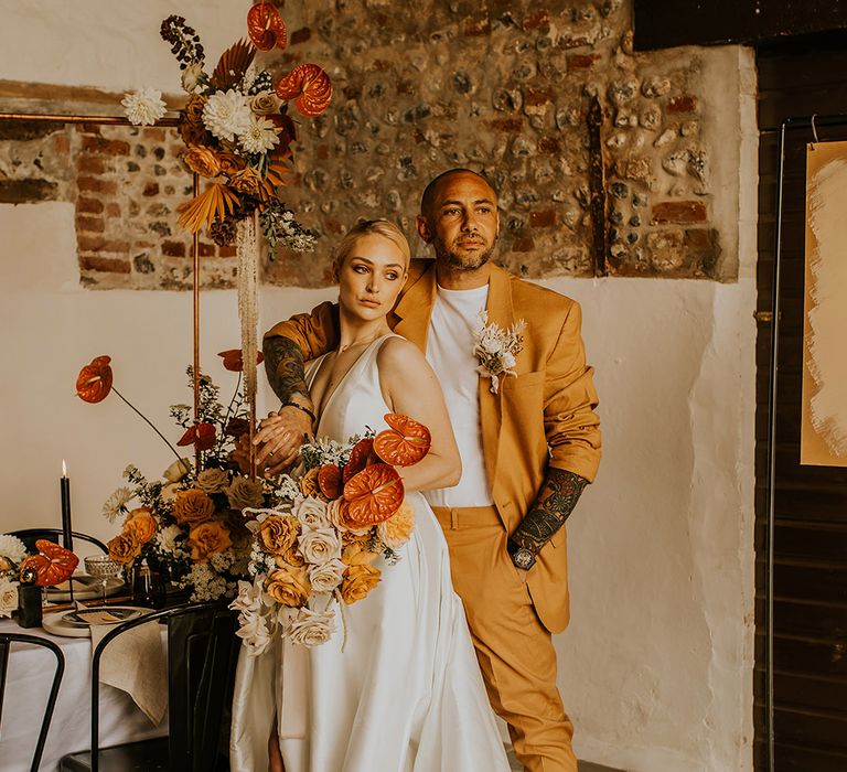 Groom in a mustard yellow suit embracing his bride in a taffeta Jesus Peiro wedding dress with long train 