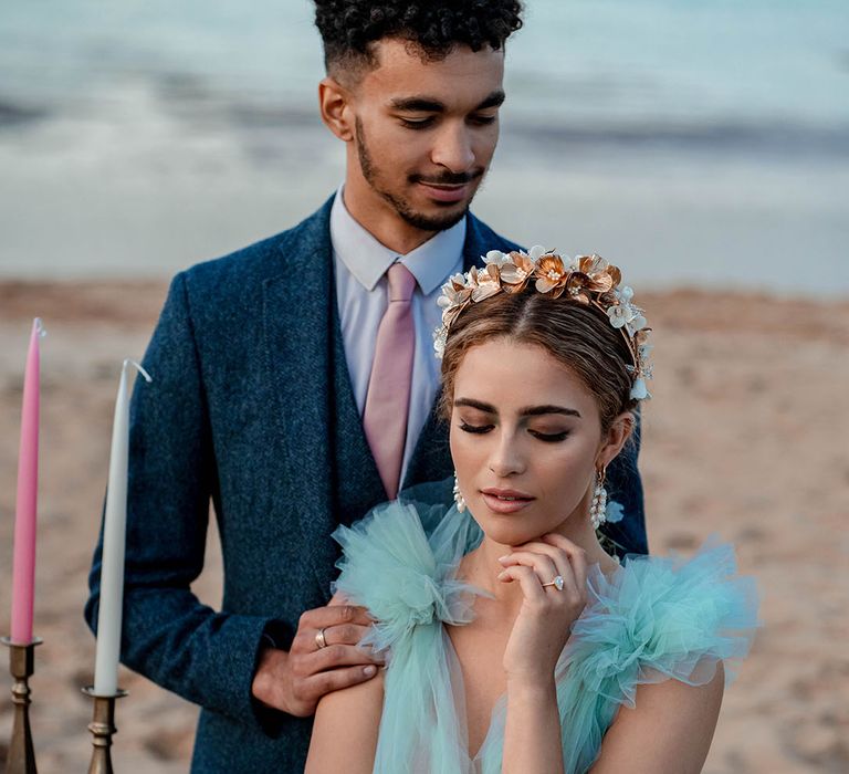 Bride in a mint green wedding dress sitting at a relaxed tabelscape on the beach with her groom in a navy blue suit and pink tie standing behind her