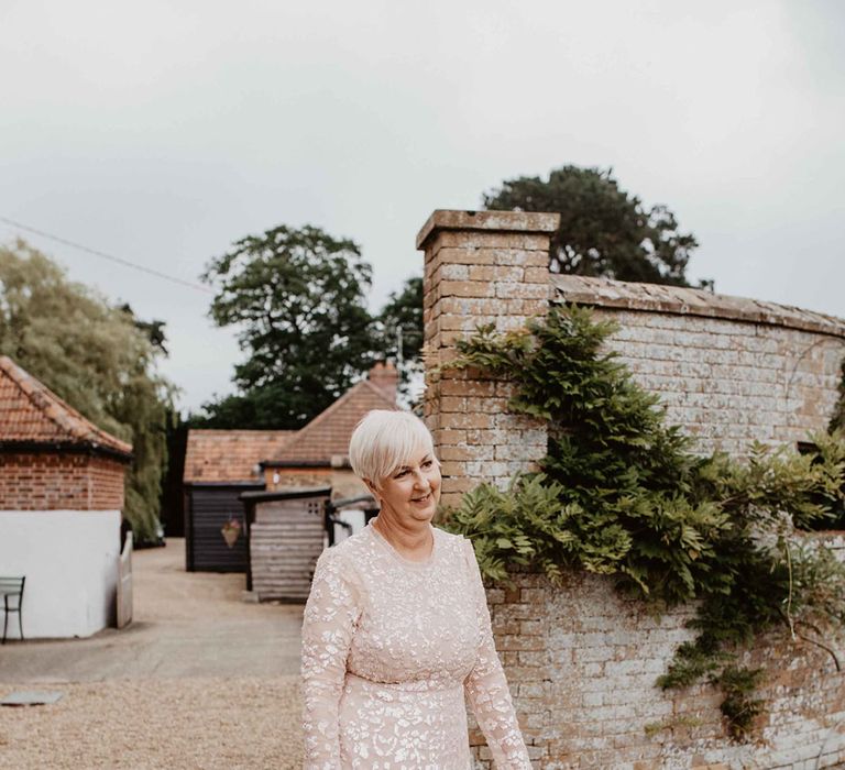 Mother Of The Bride walks outdoors wearing long gown complete with glittered floral embellishment and dusty pink hue 