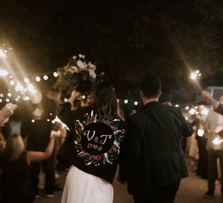 Bride & groom lean into one another as they hold sparklers with their wedding guests