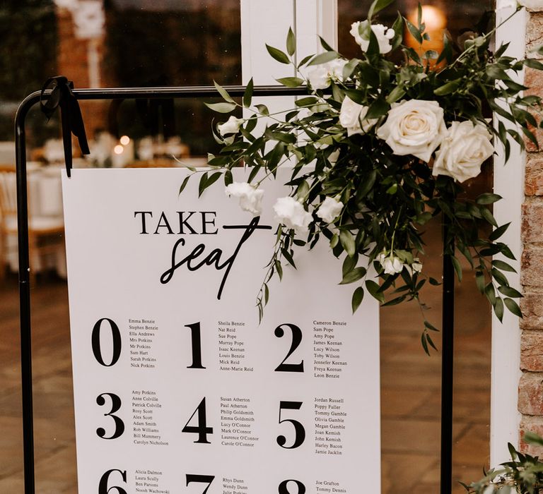 Modern wedding seating chart on a copper frame decorated with foliage 