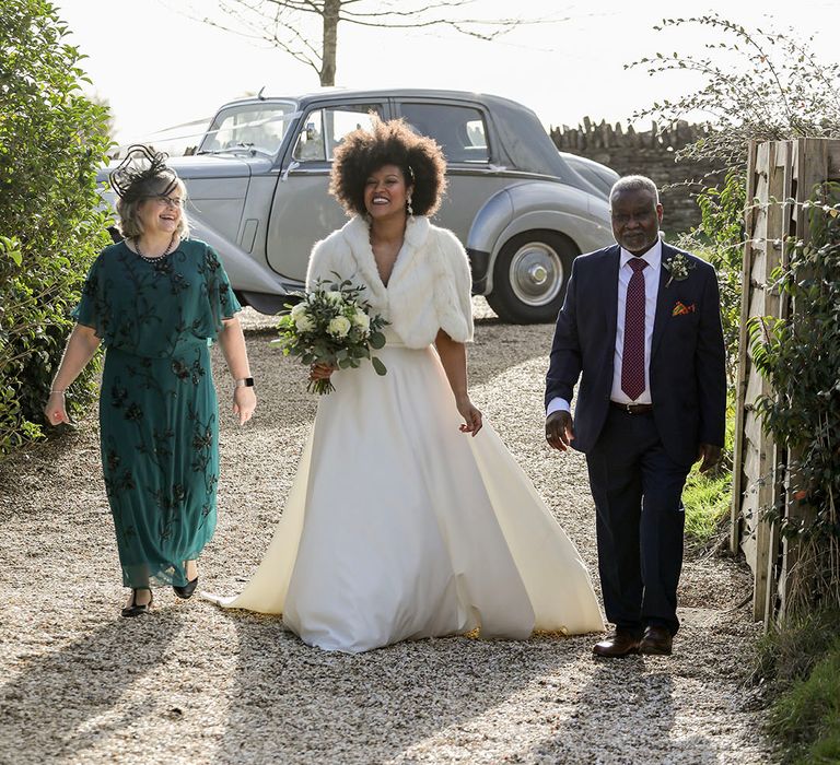 Bride walks with her mother and father outdoors on her wedding day