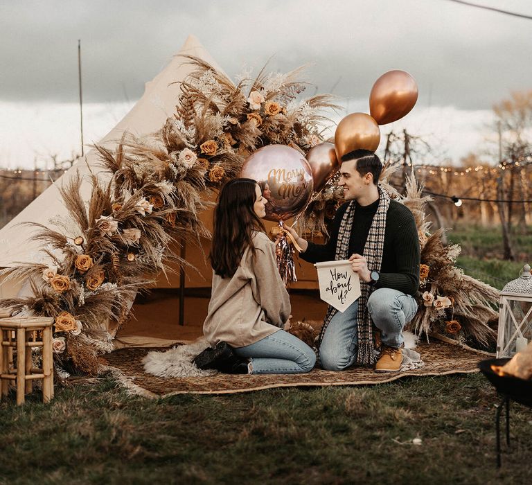 Boho campfire wedding proposal with bell tent, dried flowers, metallic balloons and fabric banners 