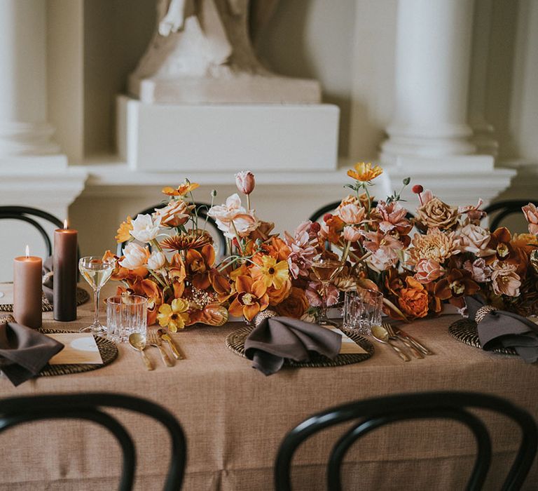 Wedding table decoration with orange, rust and mocha wedding flowers, taper candles and wicker place mats 