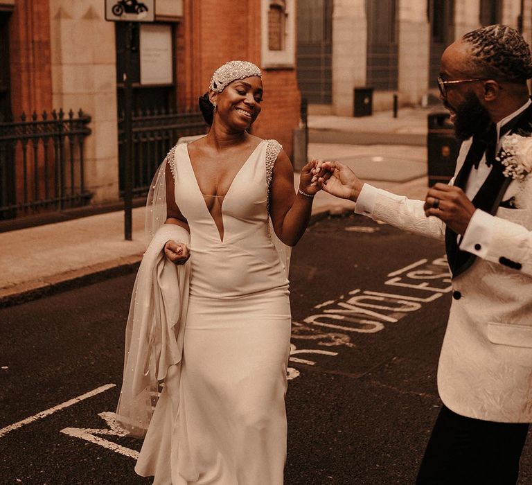 beautiful Black bride in a fitted Pronovias wedding dress with plunging neckline, silver court shoes and a beaded cap headdress