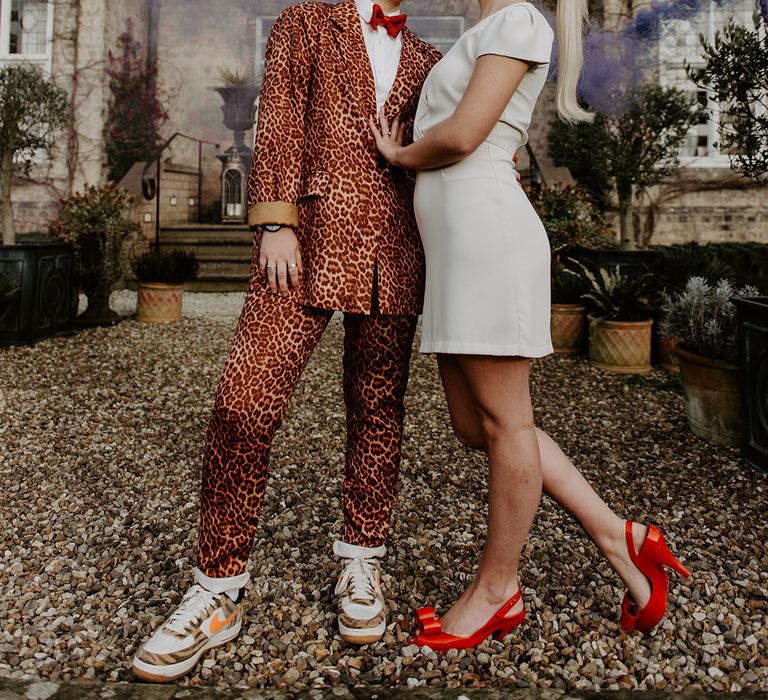 LGBTQ+ wedding with bride in a leopard print suit and trainers and a short wedding dress with bow in her hair with a purple smoke bomb going off in the background