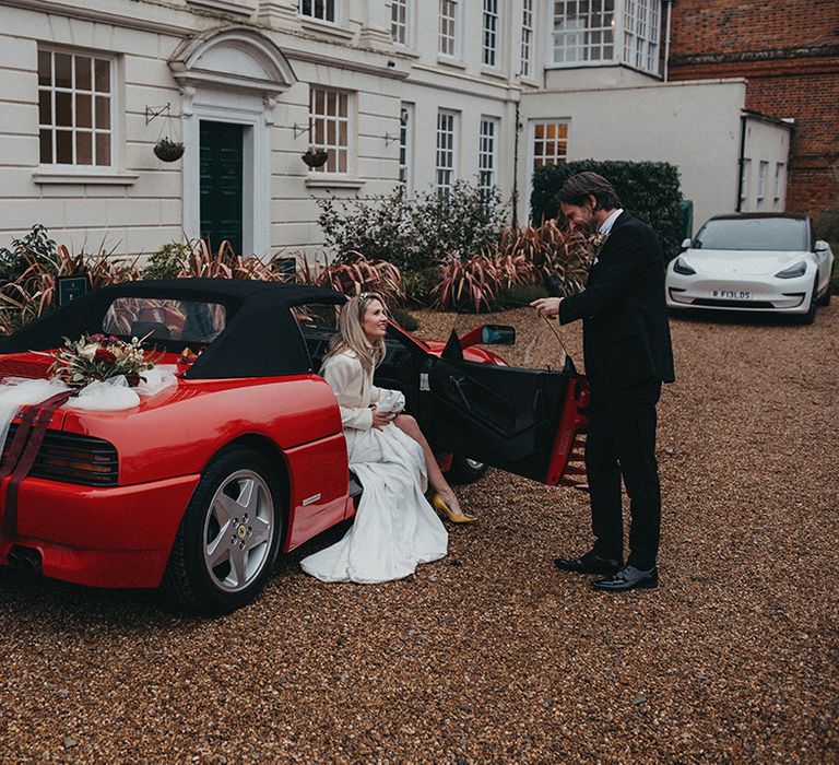 Bride sits in Ferrari as she speaks to her husband outside Gosfield Hall on their wedding day