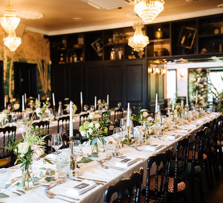 Wedding venue in Essex with hanging crystal chandeliers with forest theme wallpaper and green foliage on tables