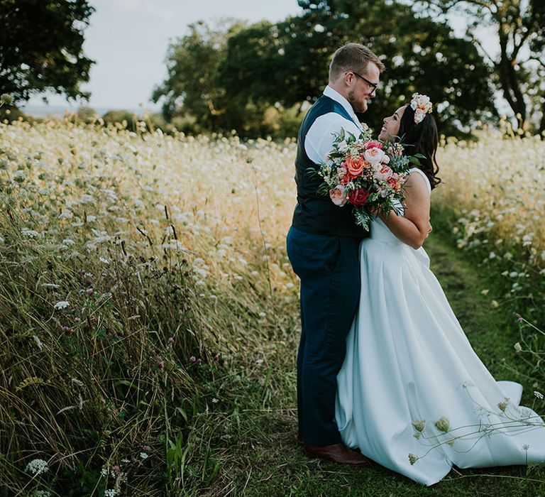 Bride and groom hug and look into each other's eyes as they stand in the countryside grounds of St Tewdrics House