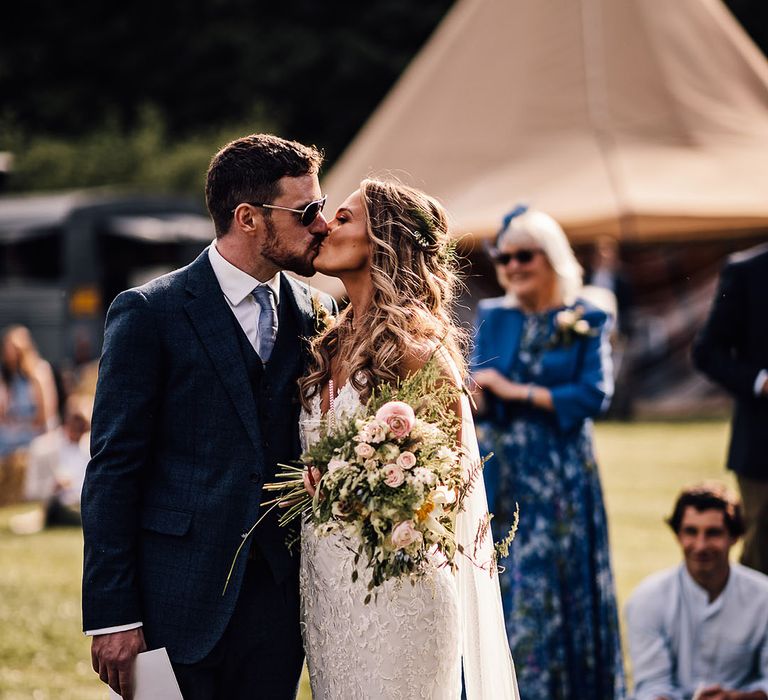 Groom in blue suit and bride in lace wedding dress share a kiss 