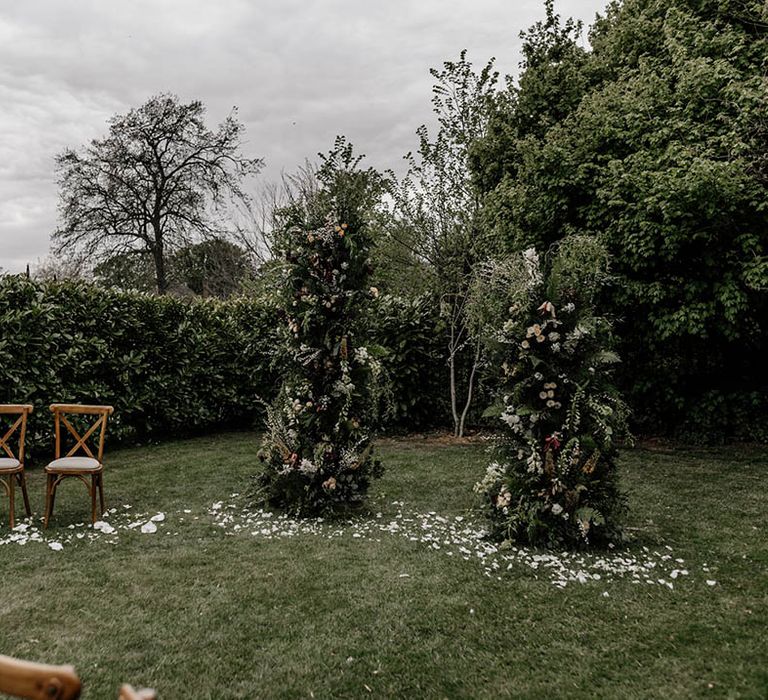 Outdoor wedding ceremony altar decor with greenery column wedding flowers and two wooden chairs