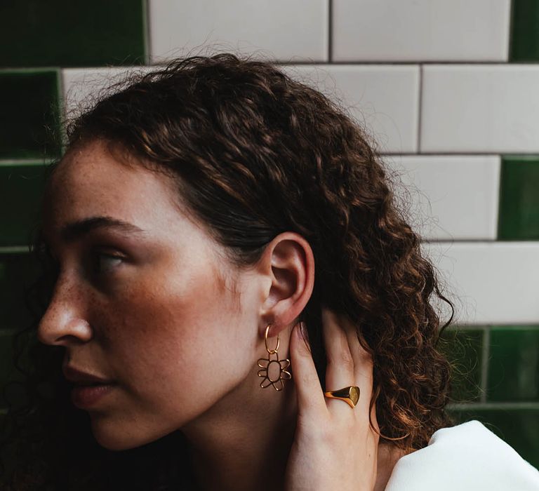 Bride with naturally curly hair and freckles wearing a gold flower earring and signet ring 