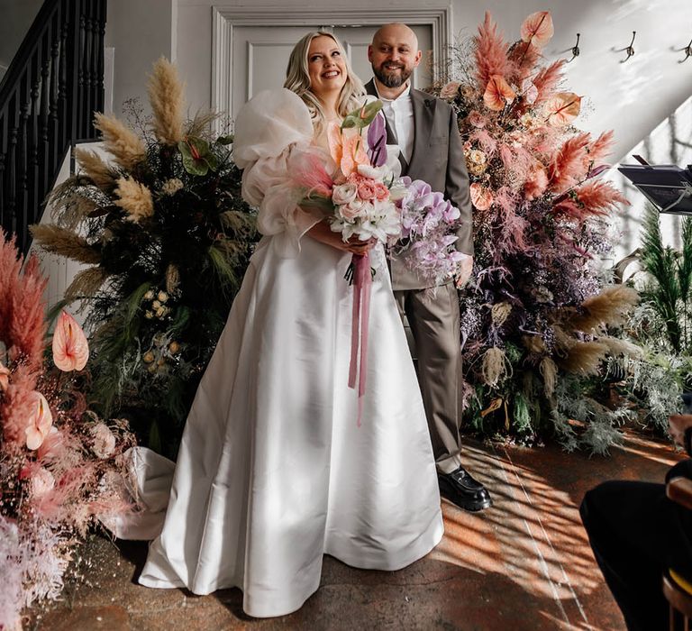 Modern stylish London wedding with dried and fresh flower column arrangements, bride in a princess wedding dress and groom in a double breasted jacket 