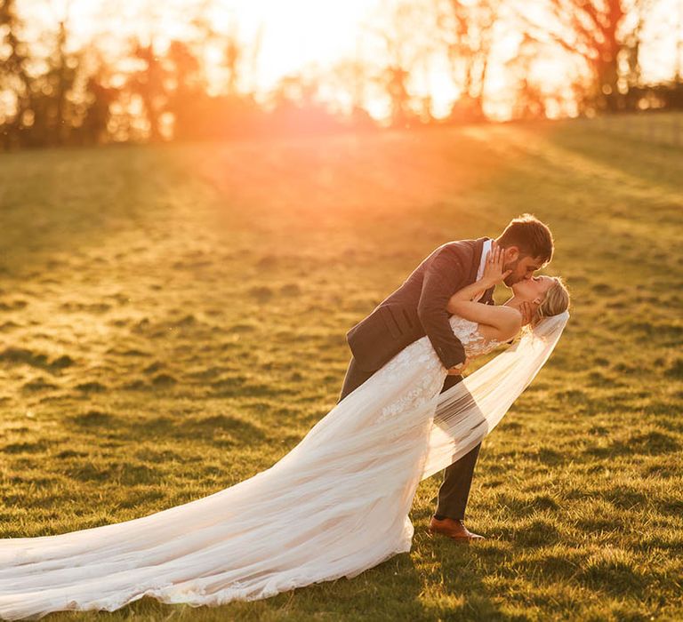 Groom in a blue suit dips the bride for a kiss during golden hour 