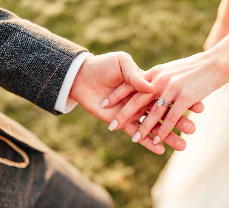 Bride with pale pink wedding nails holds hands with the groom with her diamond engagement ring and wedding band 