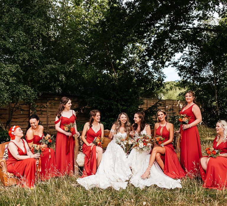 Brides seated outside surrounded by their bridesmaids in orange dresses 