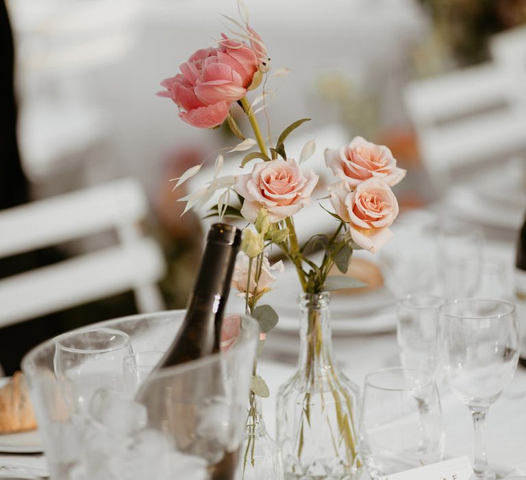 Pale pink roses and peony in glass vase on small floral arrangement across table in outdoor wedding reception