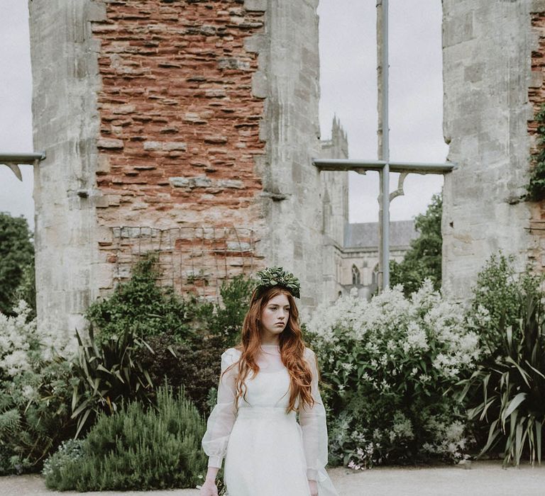 Bride in a wedding dress with sheer layer wearing a foliage flower crown standing in the gardens at Bishop's Palace, Wells