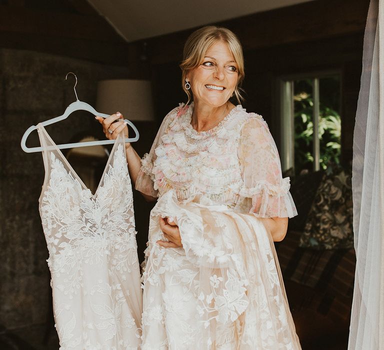 Mother of the bride in a pink floral dress holds the bride's wedding dress