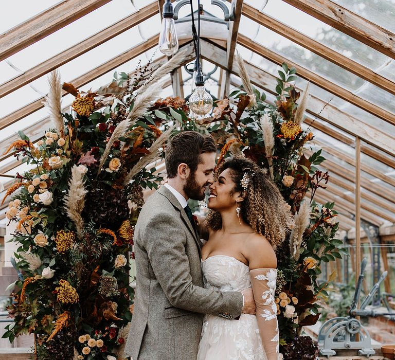 Bride and groom stand in front of autumnal wedding flower columns for glasshouse reception 