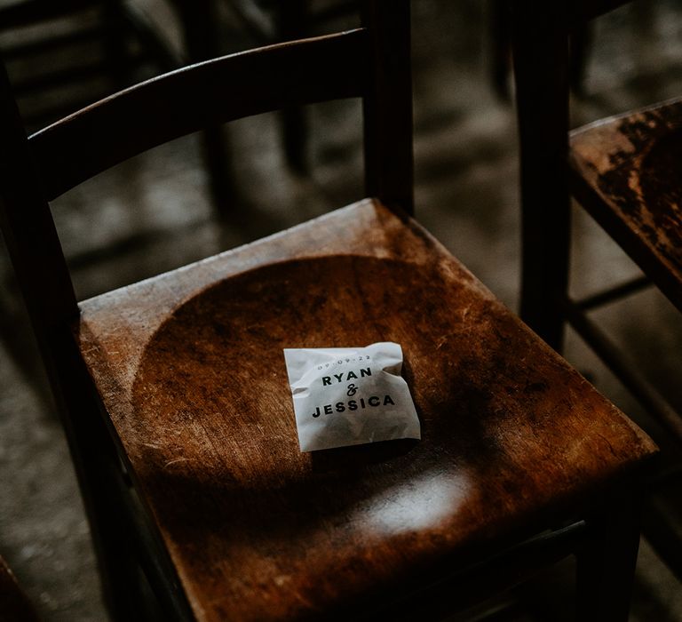 Confetti pack with the couples name on, placed on dark rustic wooden chair at alternative celestial wedding