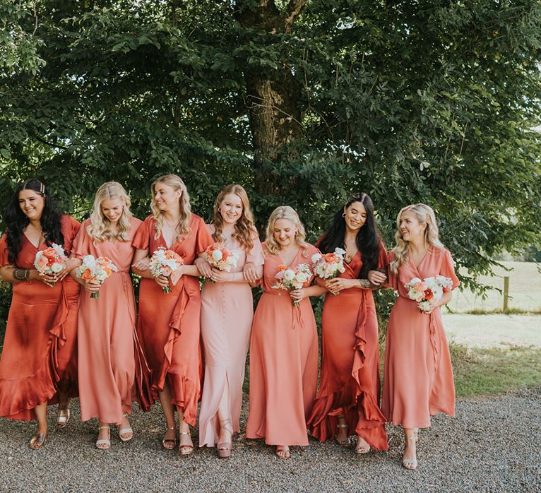 The bridesmaids all pose together in their coral peach bridesmaid dresses in various shades 