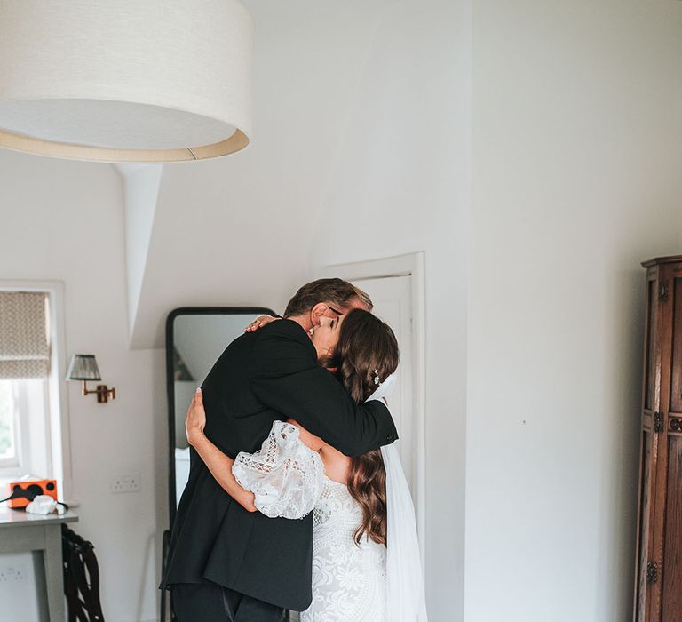 Bride in boho fitted lace wedding dress hugging her father as he sees her in her dress for the first time 