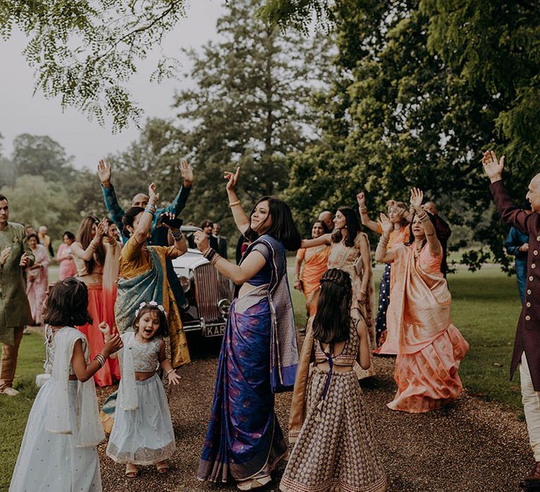 Wedding guests wear colourful outfits and dance outdoors in the gardens of Braxted Park Estate 