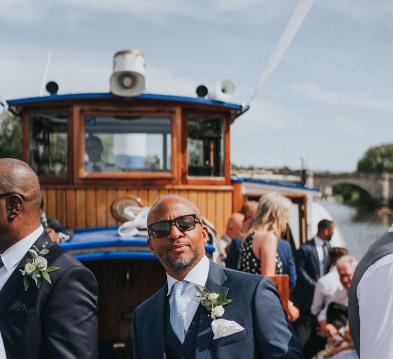 Groomsmen wears three piece suit with pale blue tie and floral buttonhole 