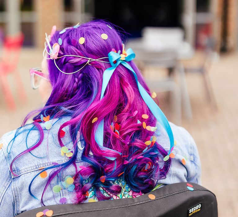 Bride with vibrant purple hair with blue bridal hair ribbon and confetti in wheelchair with blue glittery fairy wings 