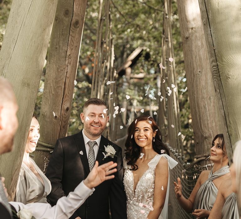 Groom in black suit with patterned tie and tie rose buttonhole with the bride in an sparkly embellished wedding dress having their confetti exit at their unique wedding venue