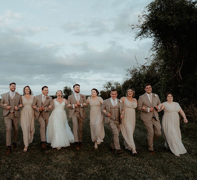 Bride & groom walk alongside their wedding party in neutral tones for festival wedding reception 