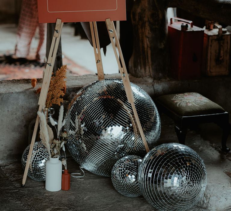 Orange and white wedding welcome sign on a wooden easel with disco ball decor and dried flowers for rustic glam wedding 