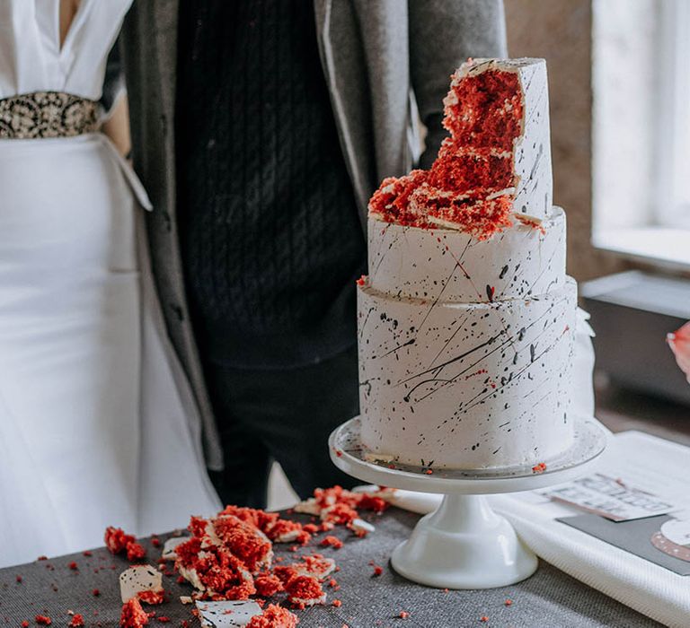 Three tier buttercream red velvet wedding cake with black paint splatter icing on contemporary, monochrome wedding tablescape 