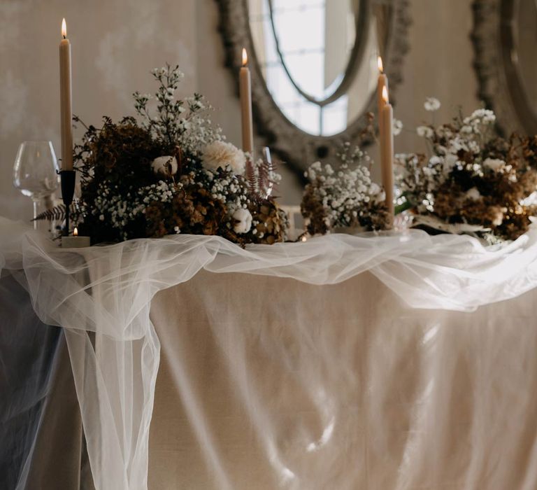 Modern luxe wedding tablescape with garden rose, baby's-breath and and dried flower table arrangements, in ceramic vases, tea light candles in ceramic candle holders and sheer tulle table runner    