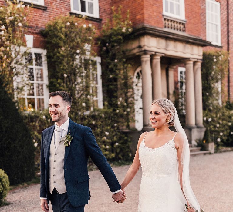 The bride in a fitted lace wedding dress with the groom in a three piece navy and grey suit at Iscoyd Park country house wedding venue 