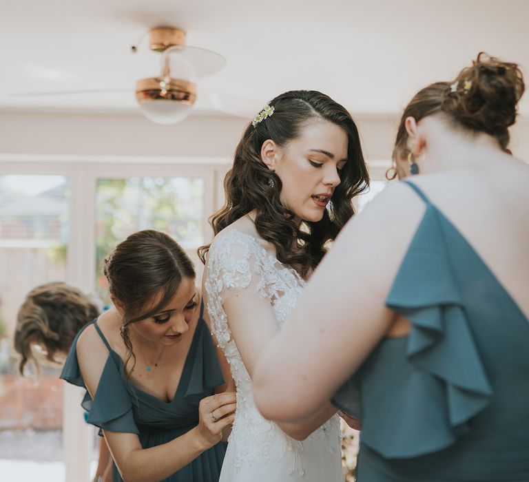 The bride gets ready for the wedding day with daisies in her hair and the bridesmaids helping her into her beaded wedding dress 