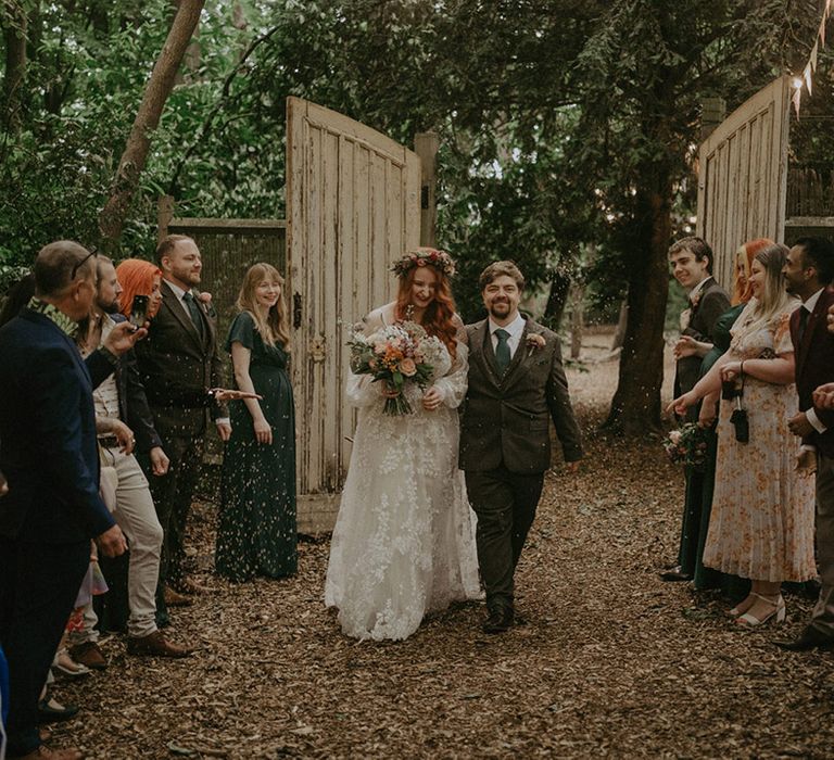 Groom in three piece suit with dark green tie has confetti moment with the bride at their outdoor woodland wedding 