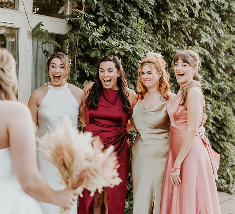 Colourful satin mismatched bridesmaid dresses worn by the bridal party who get their first look at the bride in her wedding dress 