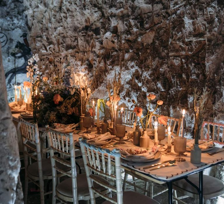 Eclectic abstract wedding tablescape with neutral toned under table cloth, abstract design wedding tablecloth on top, twisted tapered candles in ceramic candlestick holders, gold cutlery, abstract wedding stationery, and dried flower centrepieces at Margate Caves